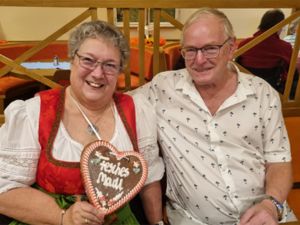 Ein Paar im Seniorenheim mit traditioneller Tracht, lachend und mit einem Lebkuchenherz beim hauseigenen Oktoberfest.